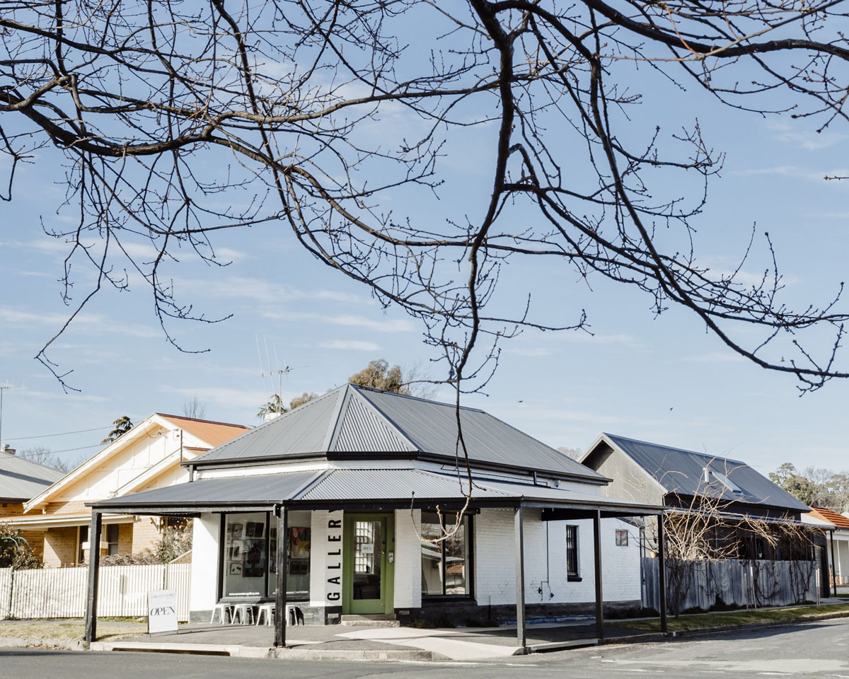 Corner gallery building with metal roof and bare tree branches.