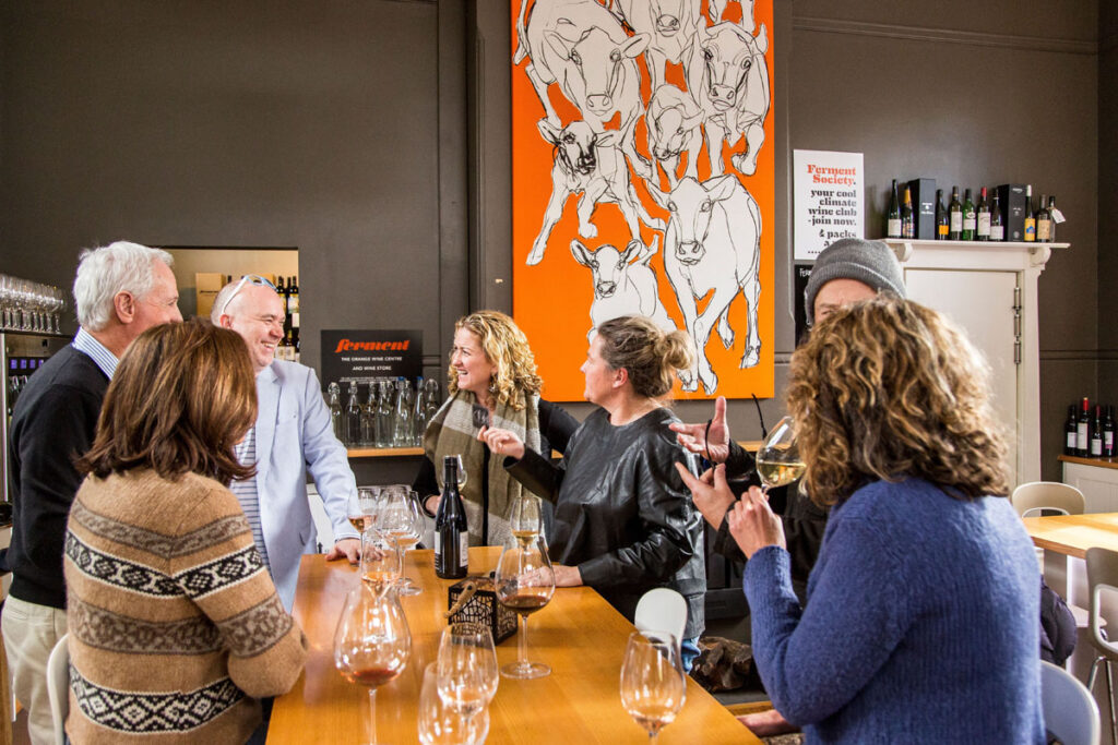Group of people tasting wine indoors with orange cow artwork in the background
