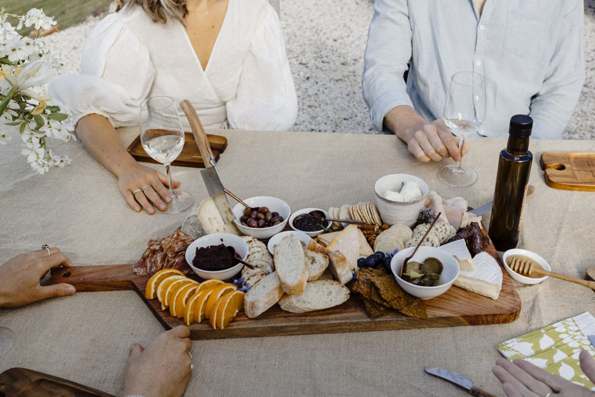 Charcuterie board with bread, cheese, olives, fruit and wine at an outdoor gathering