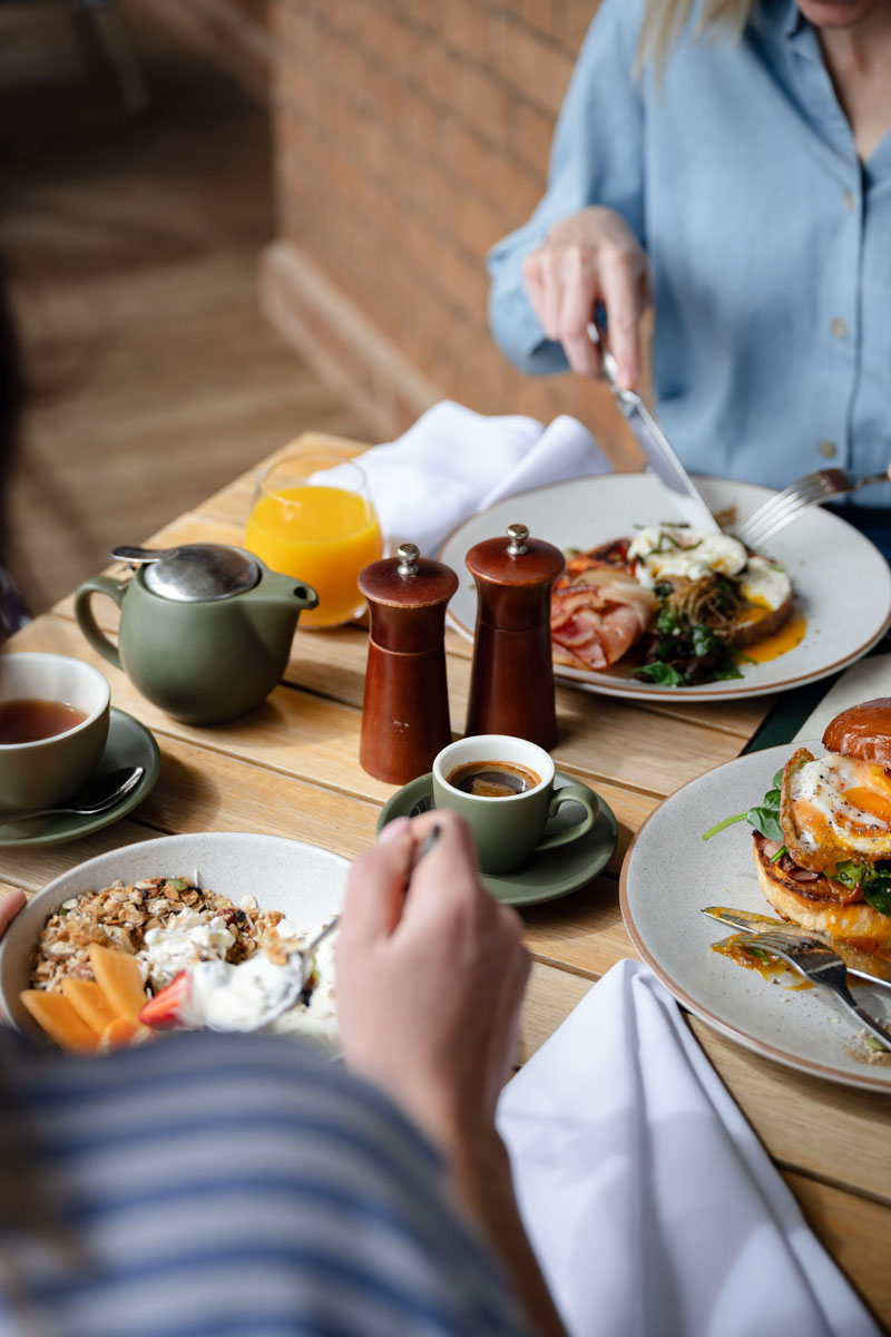 Breakfast with granola, eggs, toast, coffee, and orange juice on a wooden table