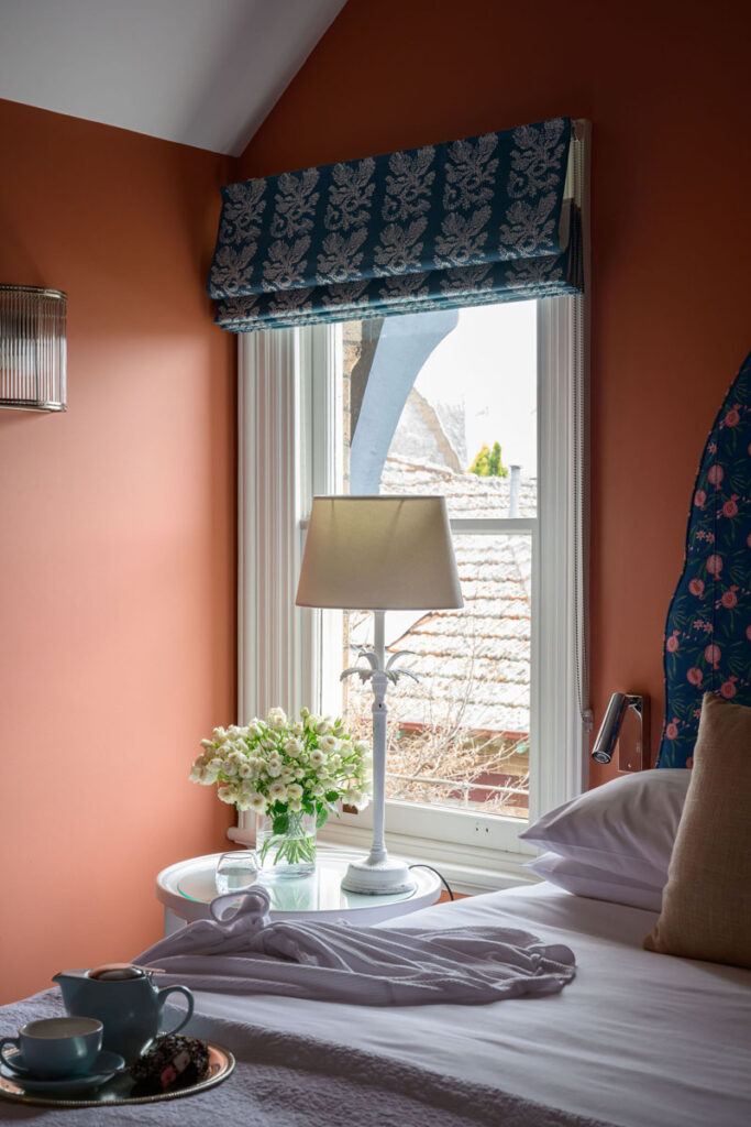 Bedroom with bed, bedside table, flowers, lamp, and window with patterned blinds