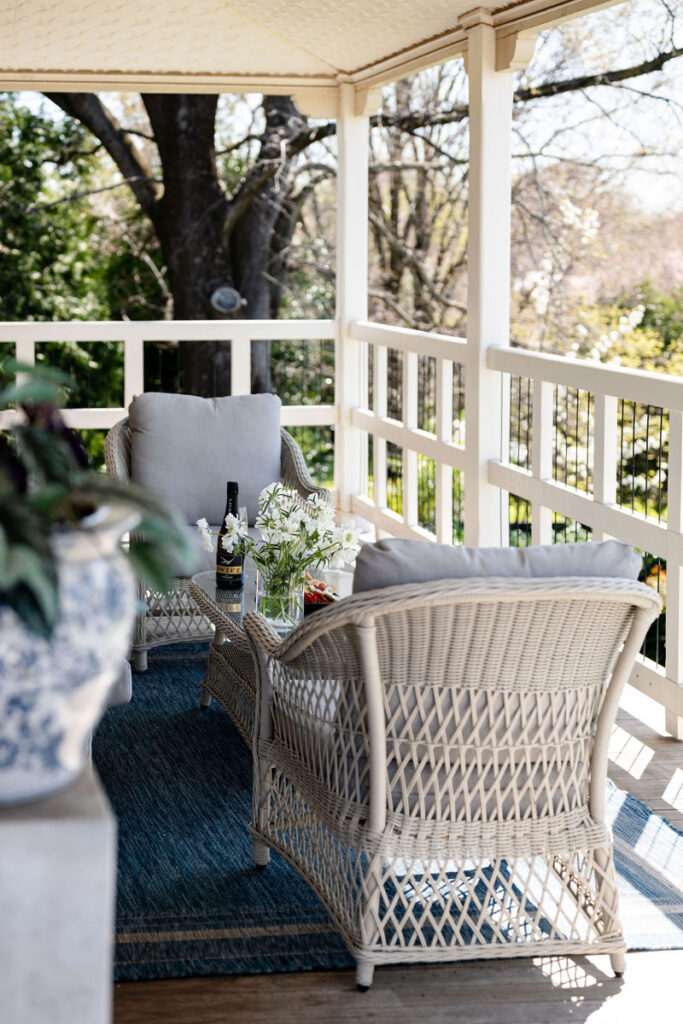 Wicker chairs with cushions on an outdoor veranda with a small table and flowers