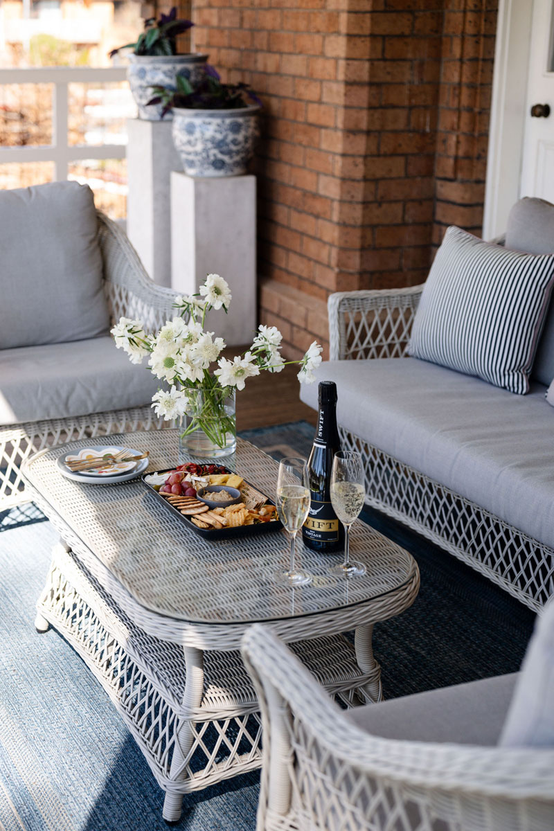 Wicker patio furniture set with snacks, champagne, and white flowers on table