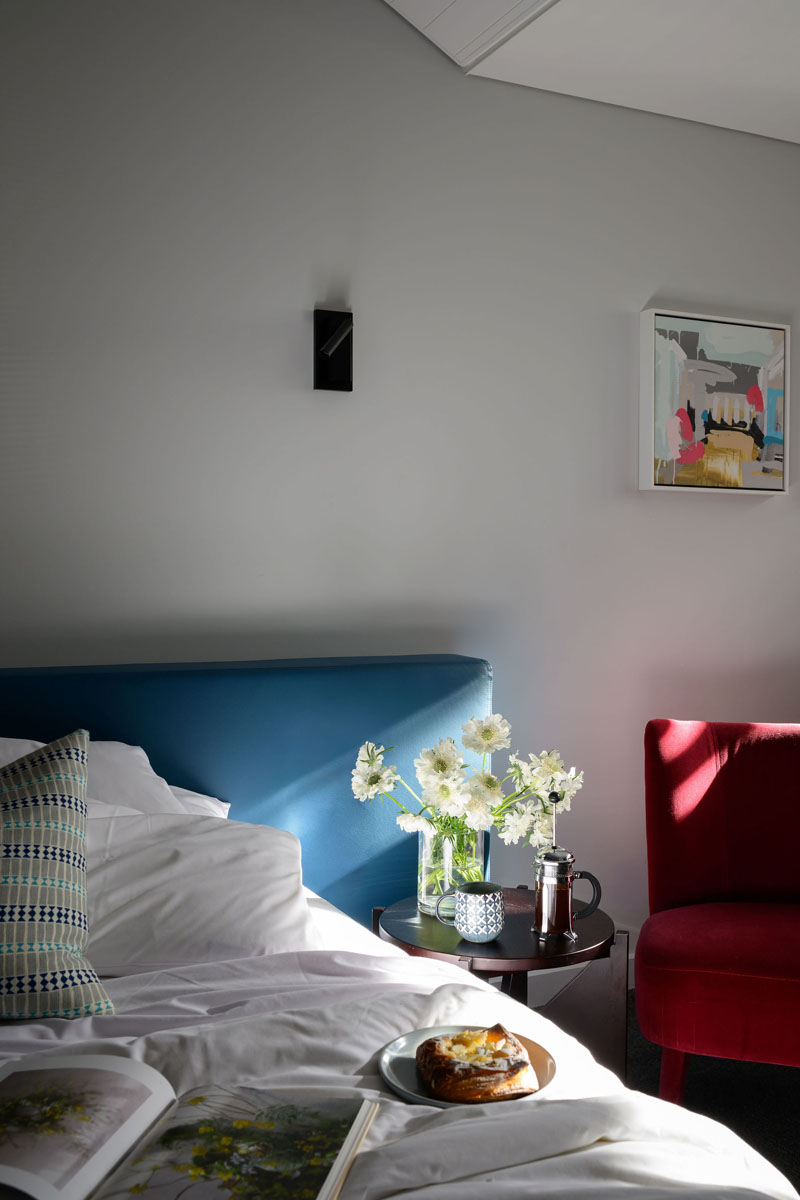 Bedroom with blue headboard, flowers on side table, and red chair