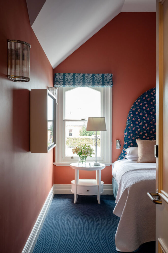 Bedroom corner with terracotta walls, white bedside table, lamp, and blue floral headboard