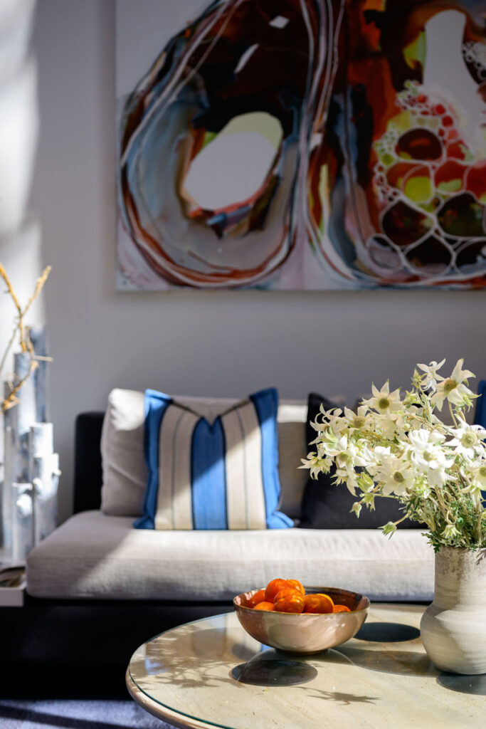 Living room with sofa, blue cushions, marble coffee table, bowl of oranges, white flowers, and abstract wall art