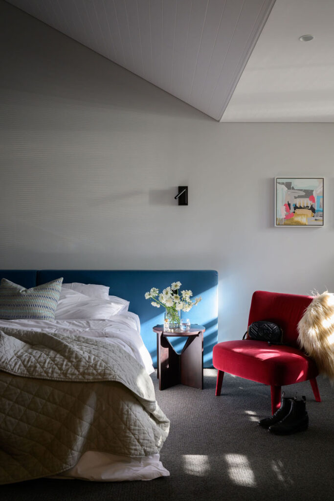 Bedroom with blue bed, bedside table with flowers, and red armchair