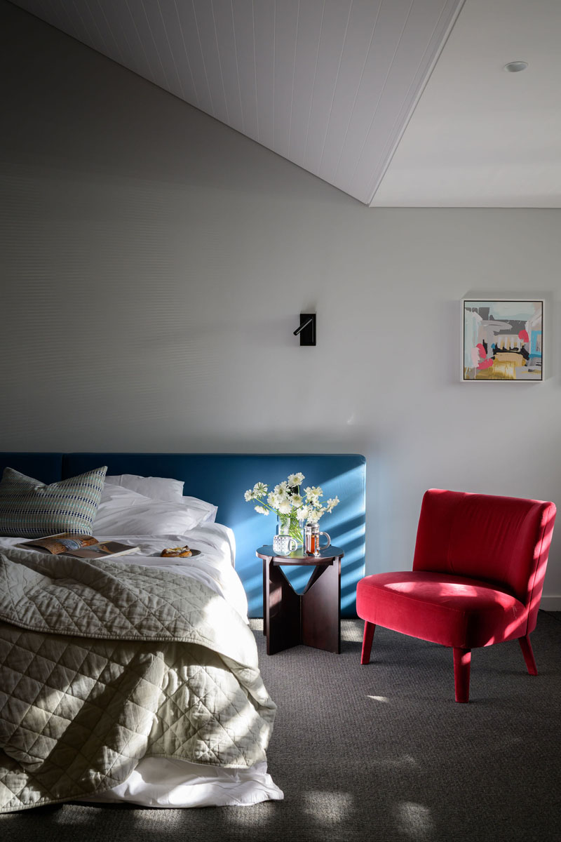 Bedroom with bed, red armchair, flowers on side table, and natural light