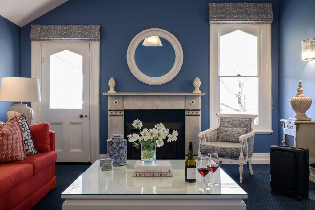 Living room with red sofa, white armchair, marble fireplace, and coffee table with flowers and wine glasses